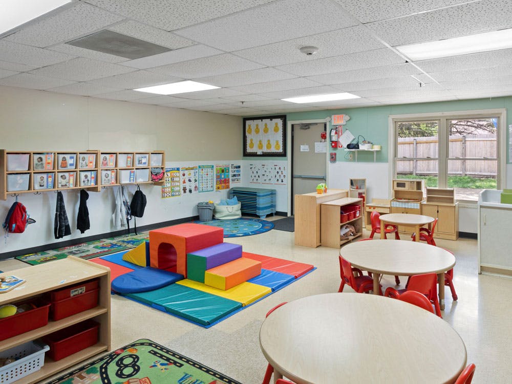 Children's classroom with small tables and chairs, cubbies, and colorful play mats