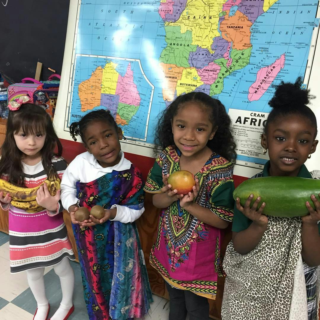 Four children holding various fruits in front of a map of Africa