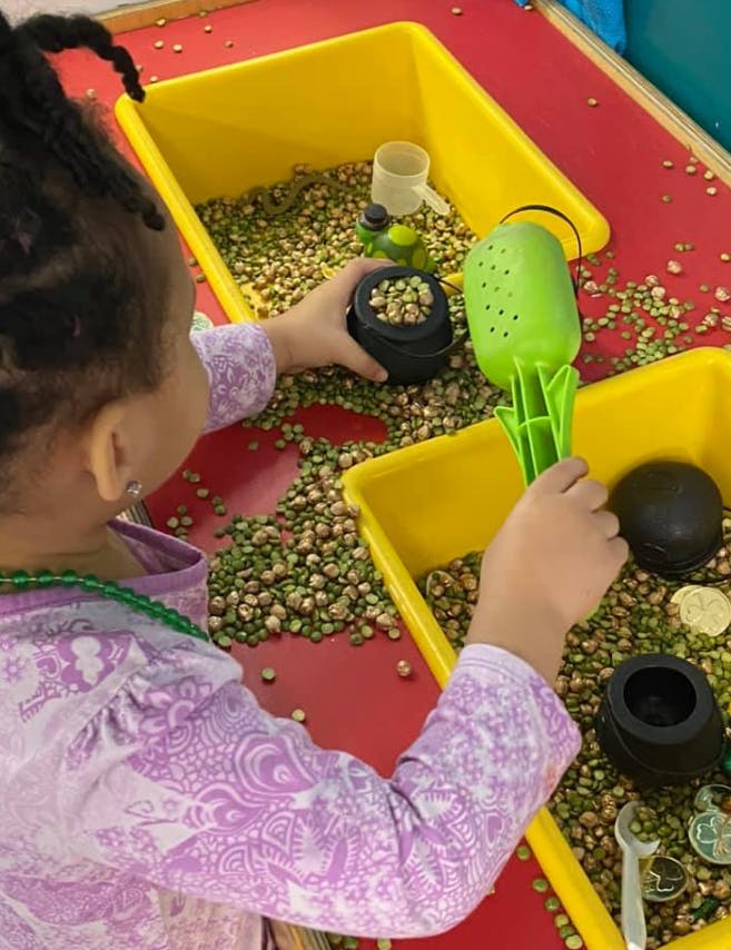 Child playing with beans and small containers in a yellow bin