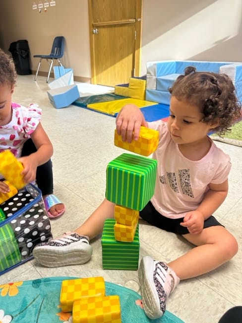 Two children playing with large building blocks on the floor
