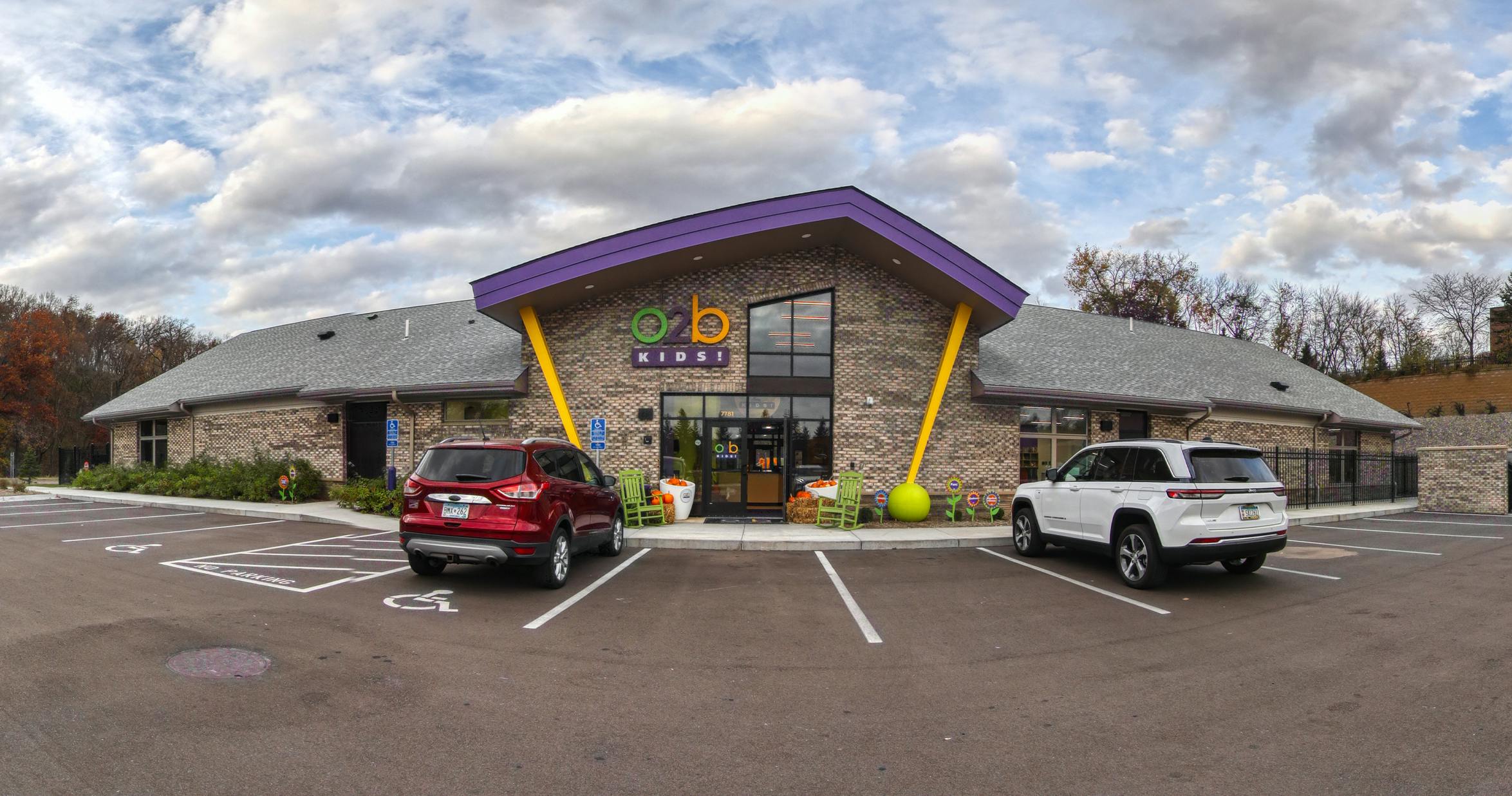 Brick building with a purple and yellow entrance, two cars parked outside