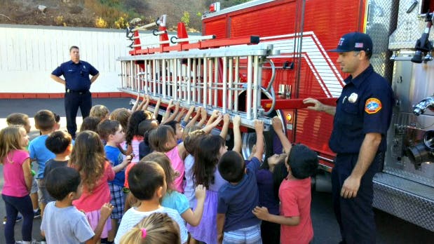 Firefighter showing children a ladder on a fire truck