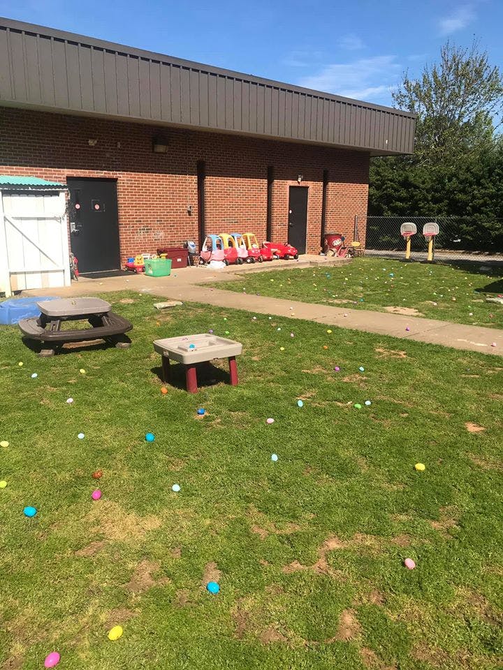 Outdoor play area with a brick building, ride-on toys, and colorful balls on the grass