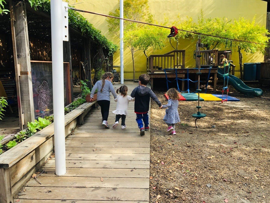 Four children walking on a wooden path towards a playground