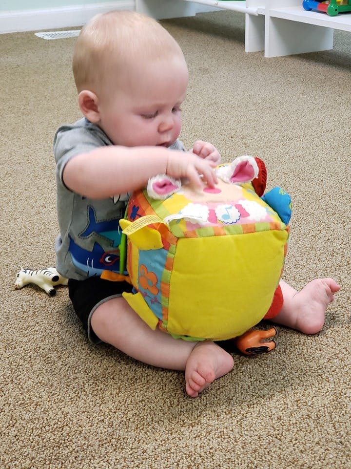 Child sitting on floor playing with a colorful soft toy