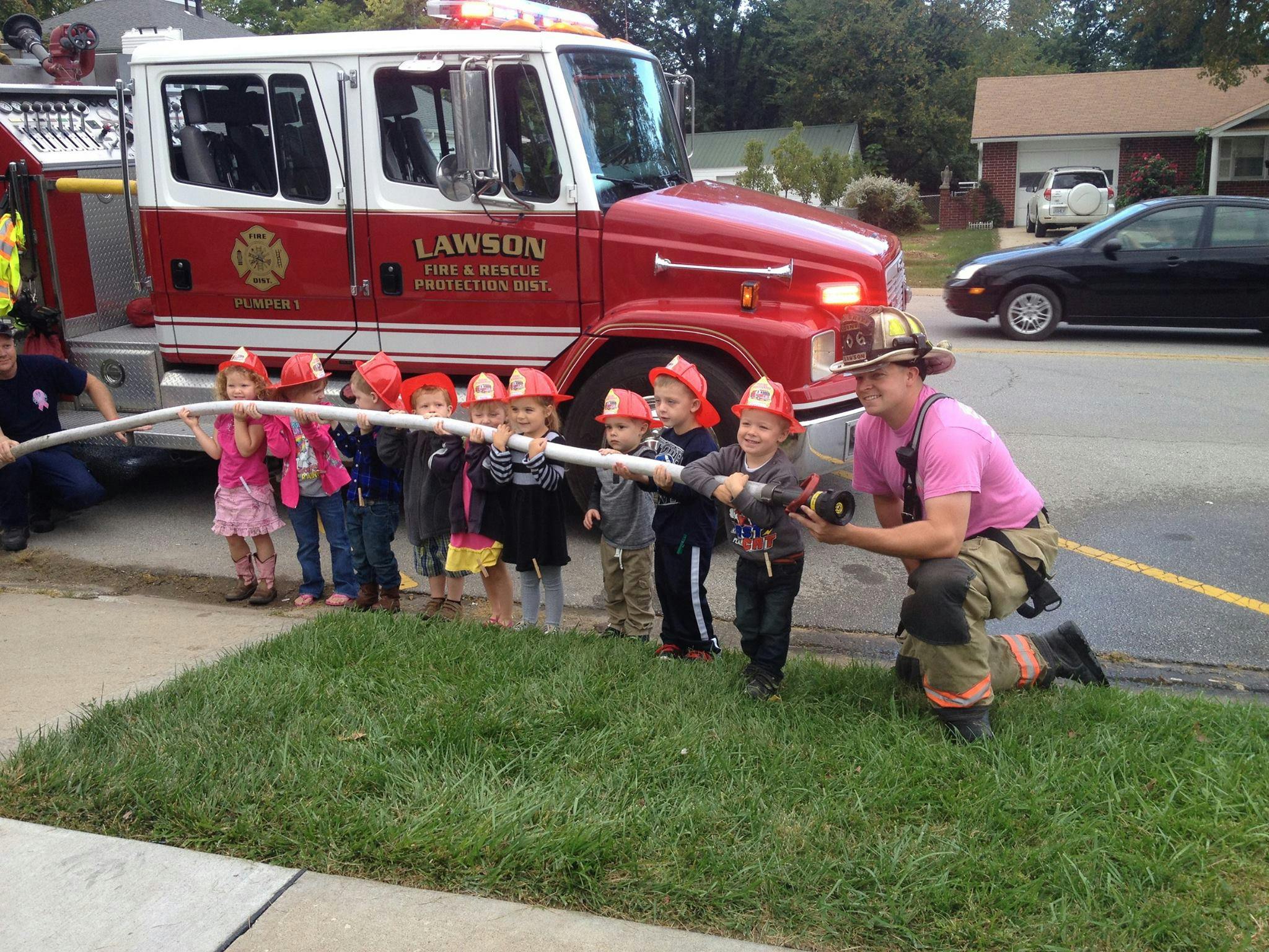 Firefighter helping children hold a fire hose next to a fire truck
