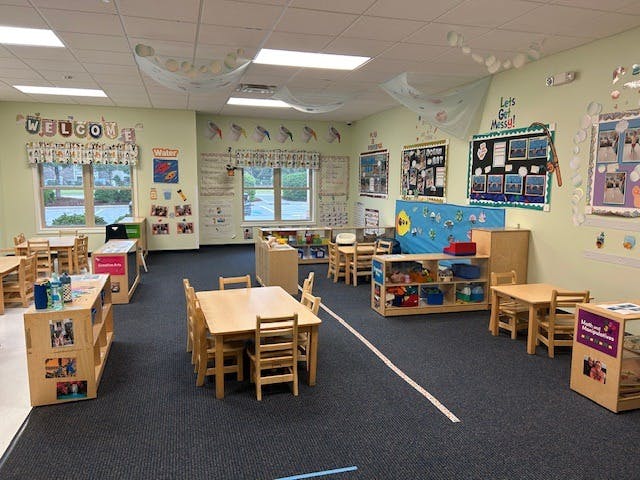 A classroom with small tables and chairs, shelves, and decorations on the walls