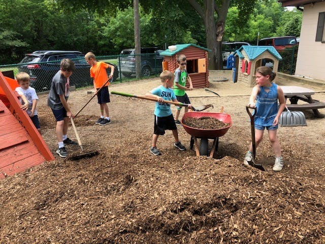 Children raking and shoveling wood chips into a wheelbarrow