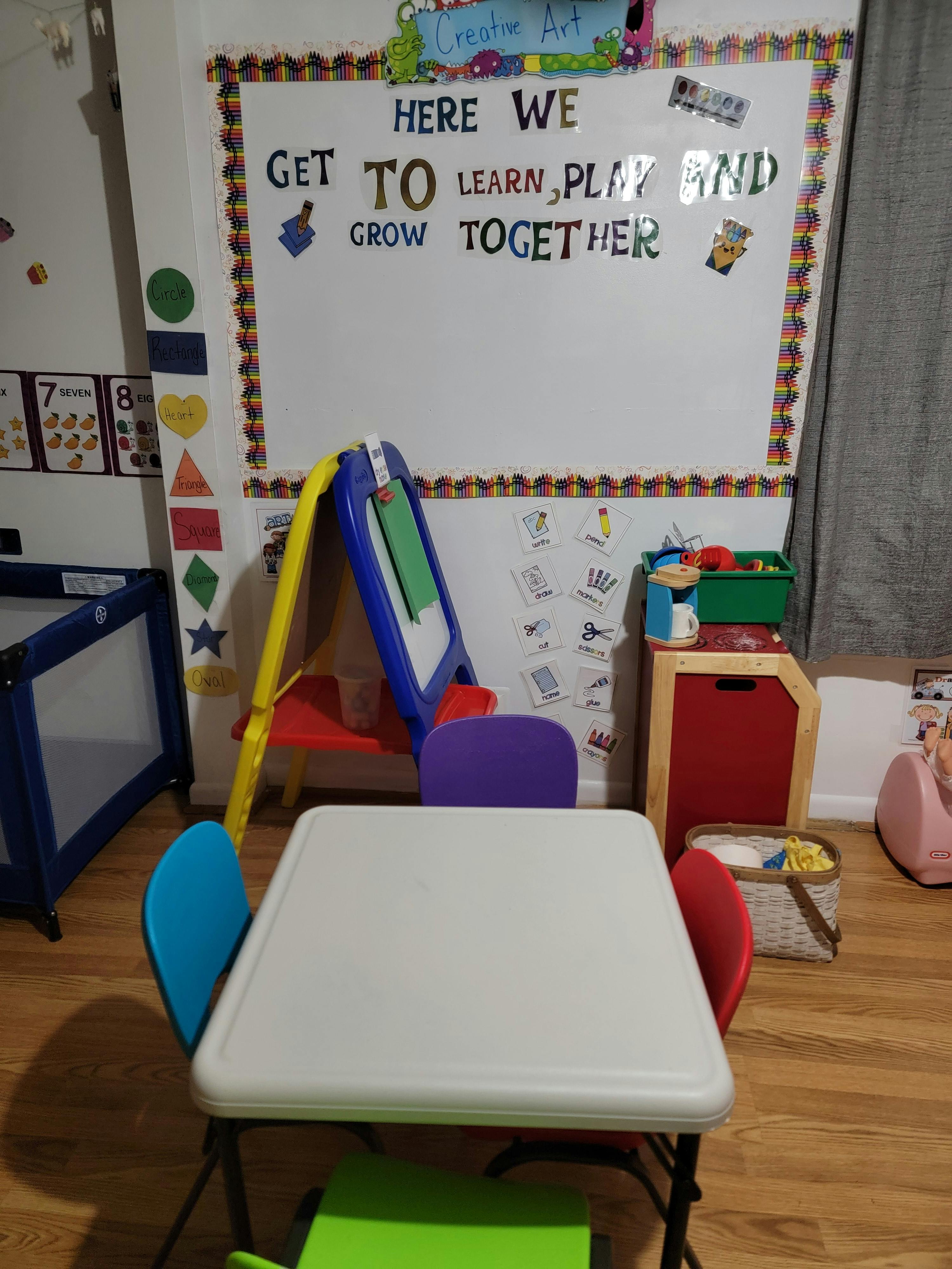 Children's classroom with a whiteboard, table, chairs, and playpen