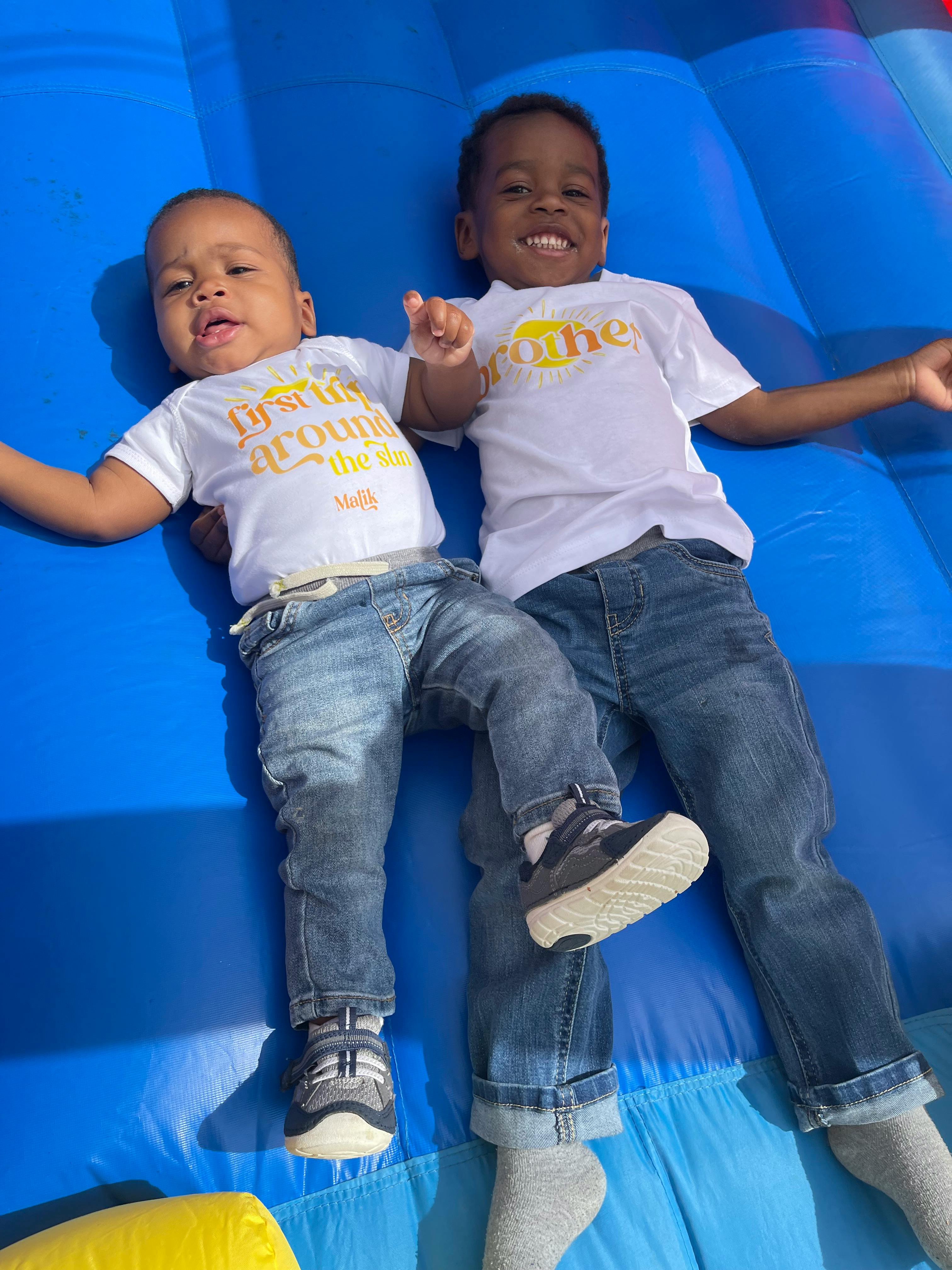 Two children in white shirts and jeans lying on a blue inflatable surface