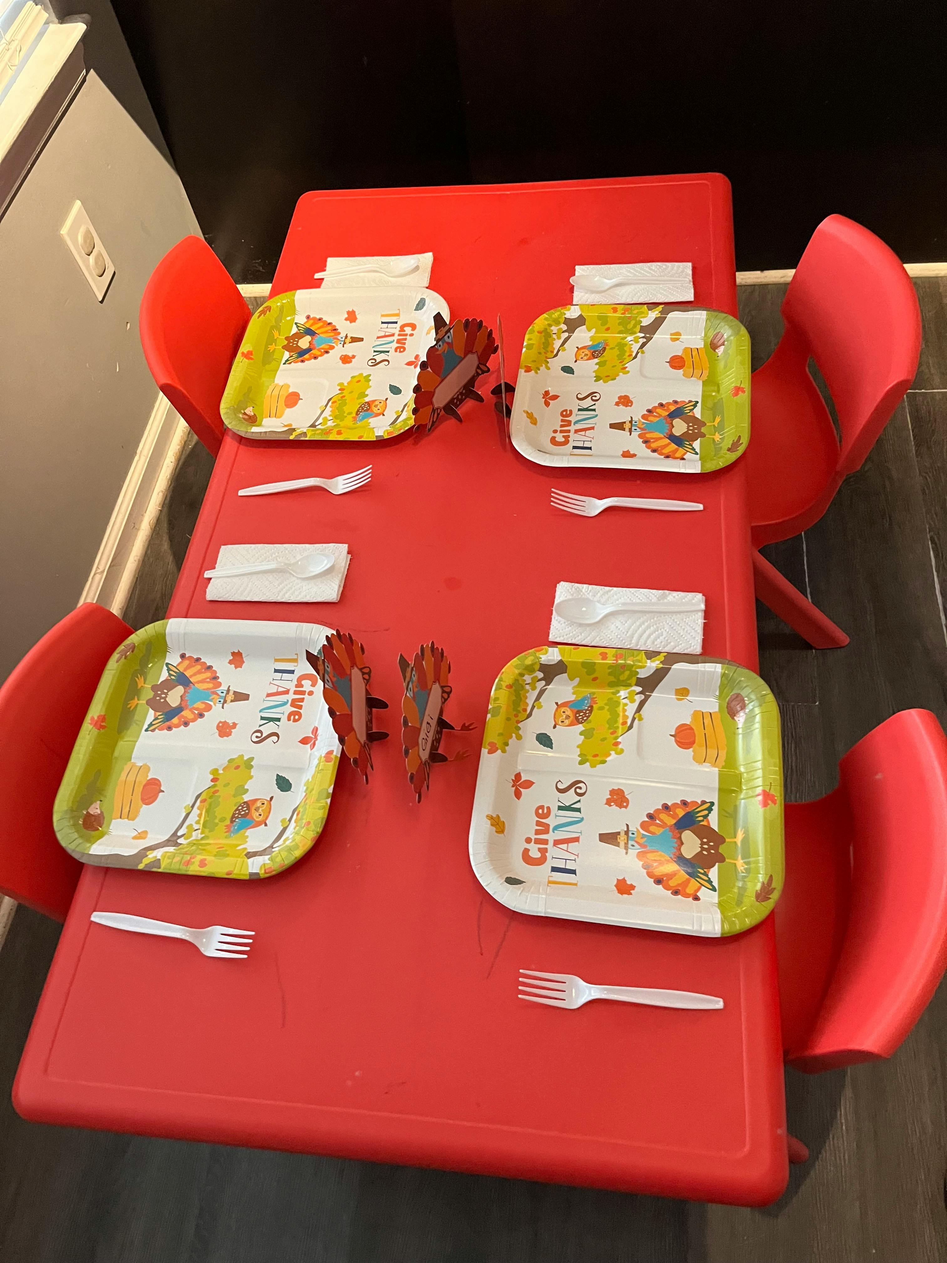Red table set with four turkey-themed paper plates, forks, and napkins