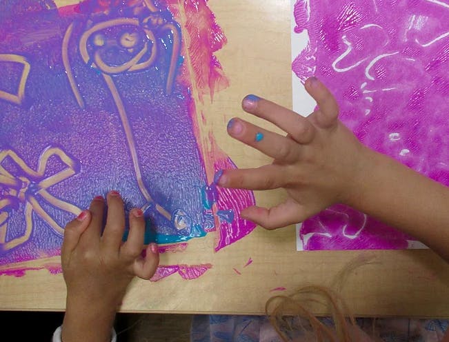 Child's hands finger painting with purple and pink paint