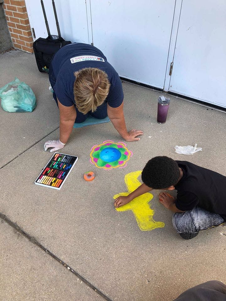 Two people kneeling on pavement drawing with chalk