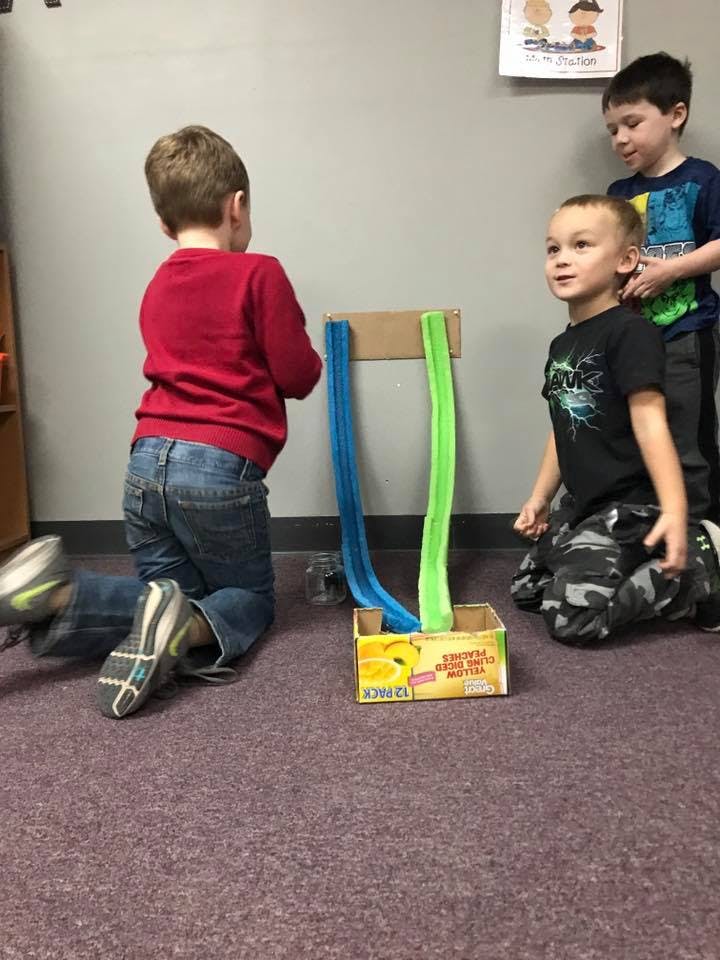 Three children playing with a homemade ramp and box on the floor