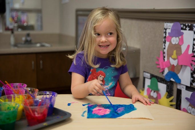 Child painting at a table with colorful paints