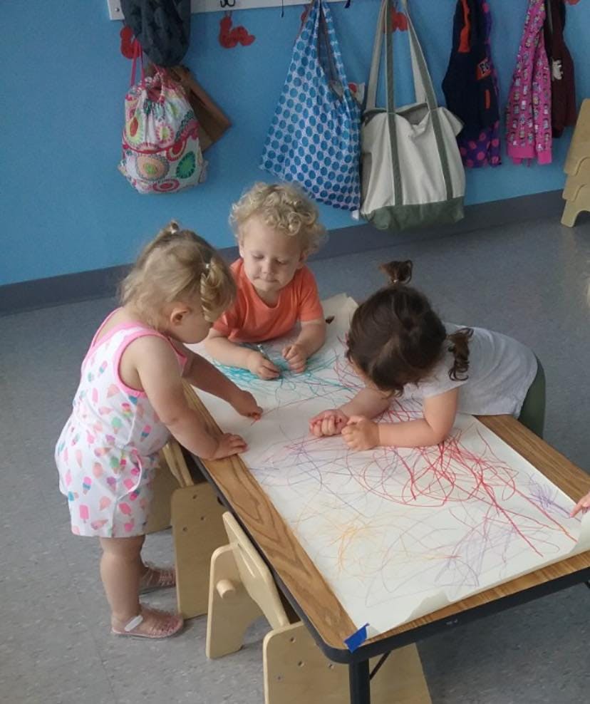 Three children drawing on a large sheet of paper on a table