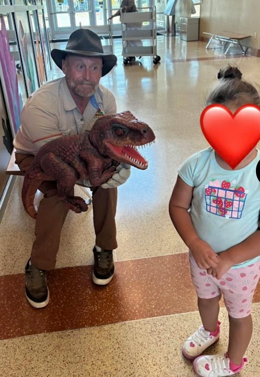 Person wearing a hat holding a dinosaur puppet near a child