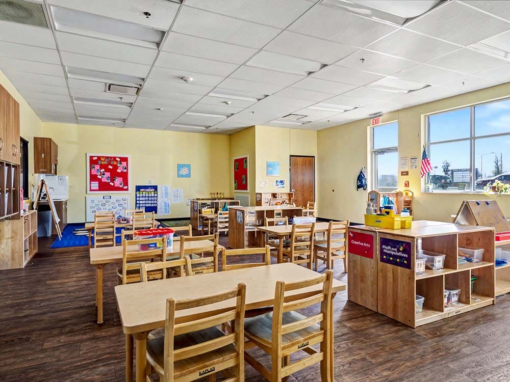 Empty classroom with small wooden tables and chairs, and bright yellow walls