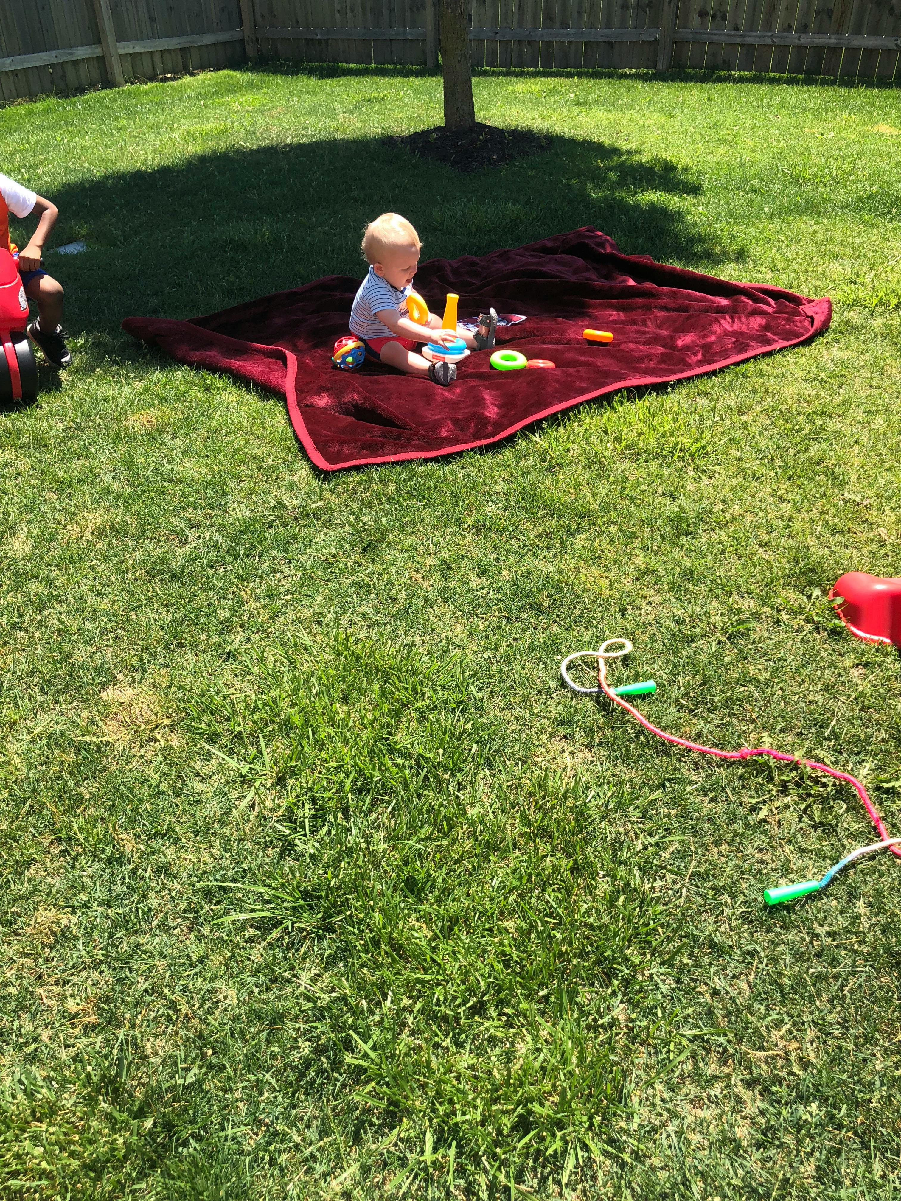 Child sitting on a blanket on the grass playing with toys