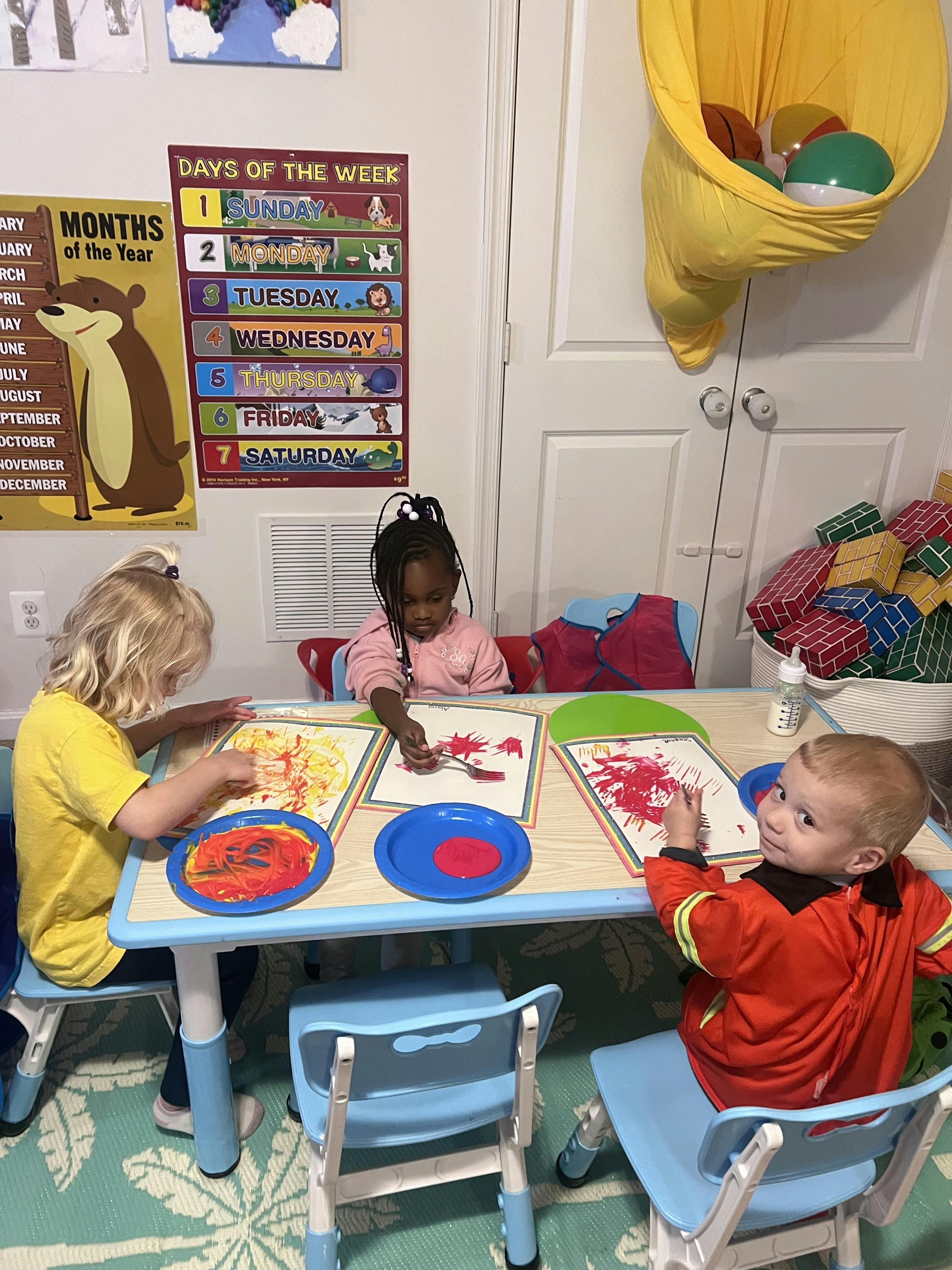 Three children sitting at a table doing finger painting