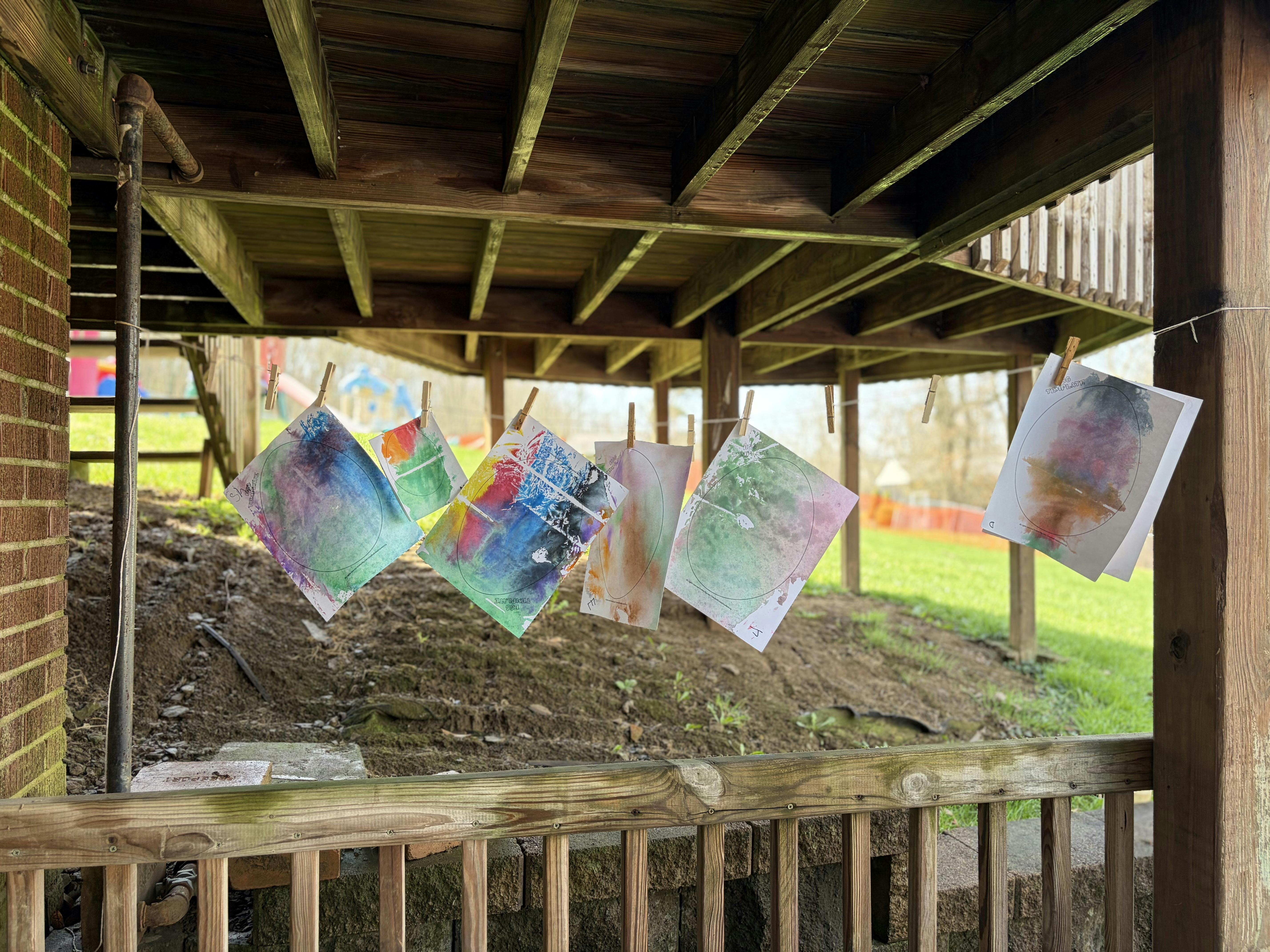 Colorful paintings on paper hanging to dry on a clothesline under a deck