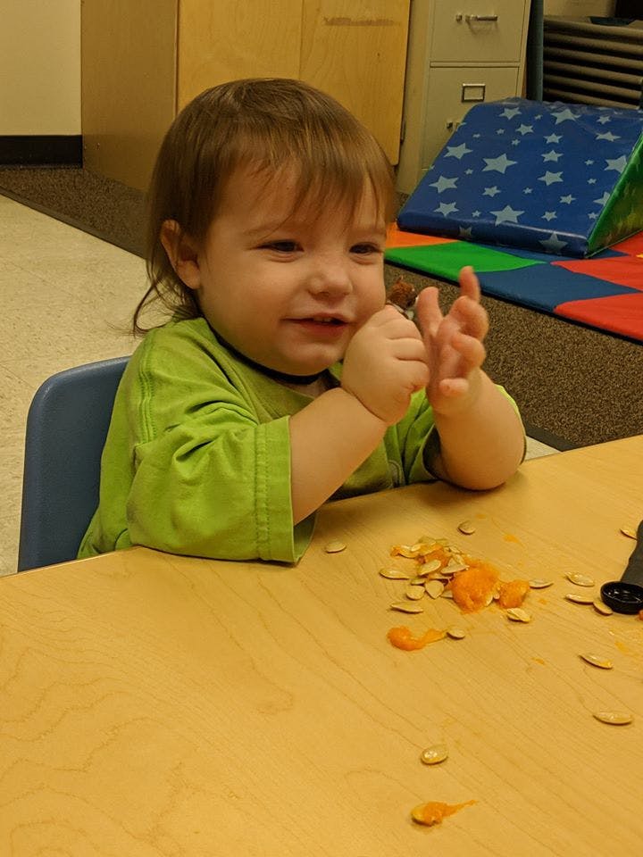 Child sitting at a table with pumpkin seeds and pulp