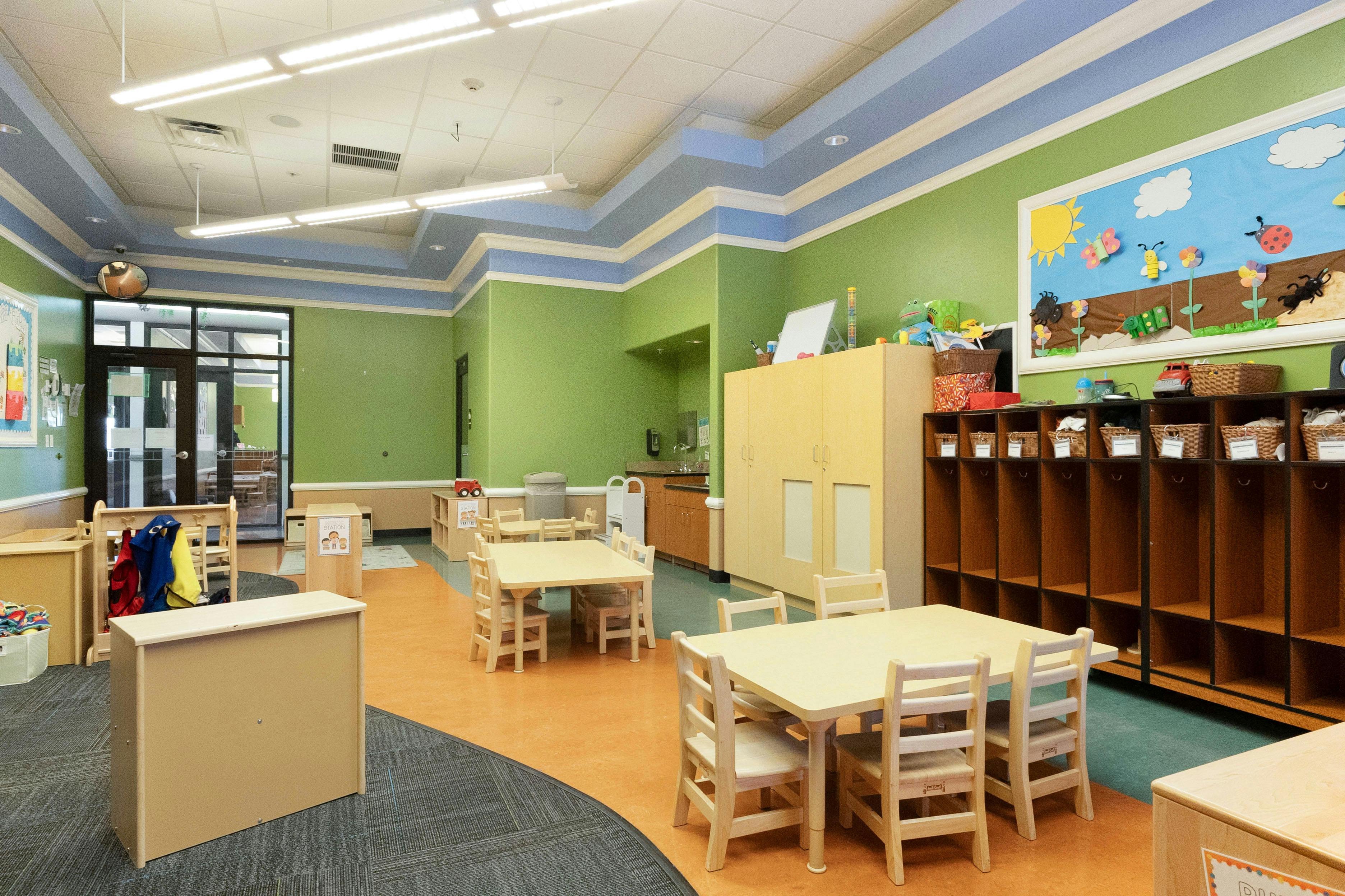 Empty colorful classroom with small tables and chairs, cubbies, and a bulletin board