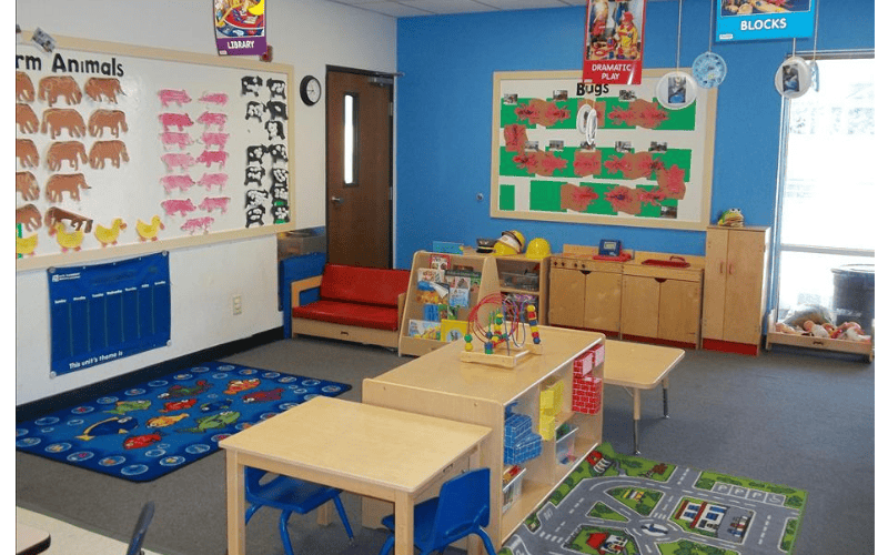 Classroom with child-sized tables and chairs, a play kitchen, and animal cutouts on a whiteboard