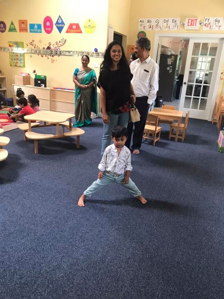 Child standing with legs apart in a classroom with adults and other children