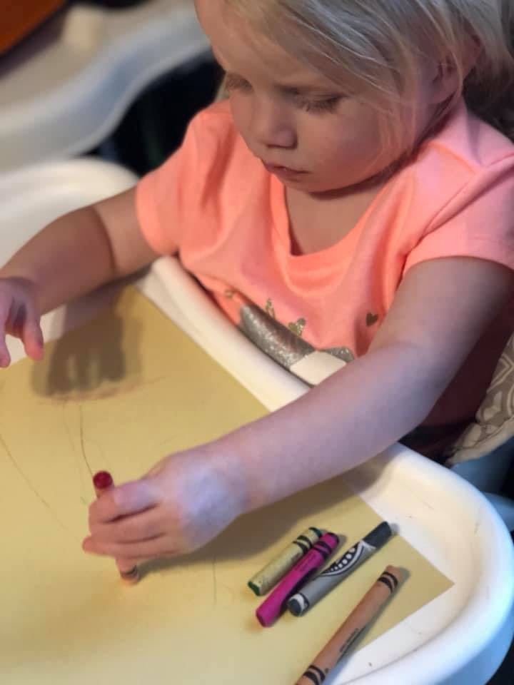 Child drawing on paper with a red crayon
