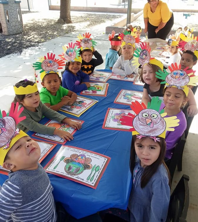 Children wearing turkey hats sitting at a table with drawings