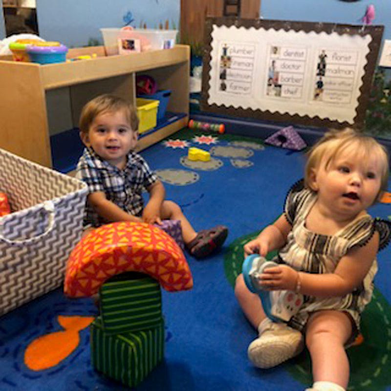 Two children playing on a blue mat in a classroom
