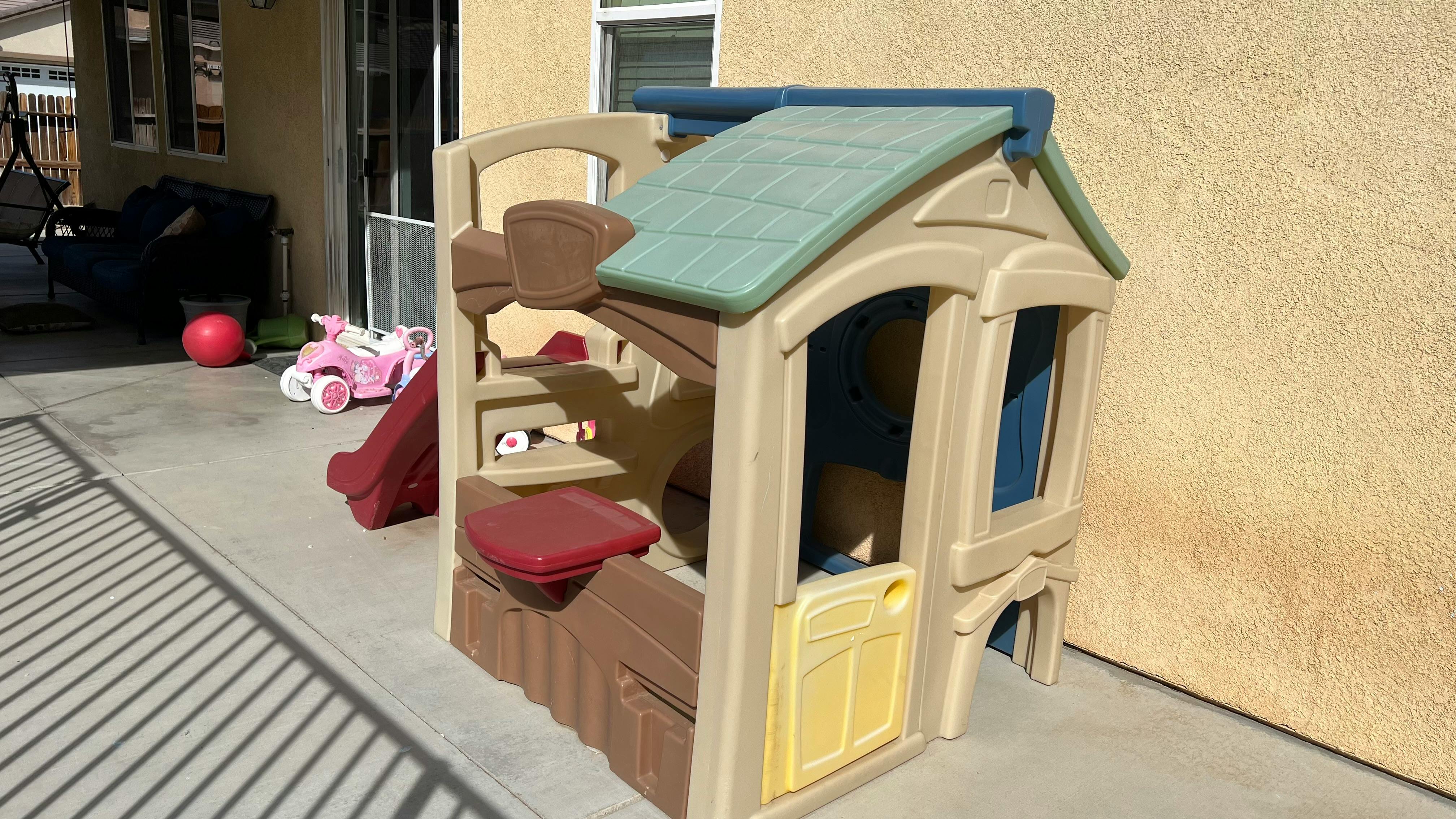 Plastic playhouse with slide and other toys on a patio