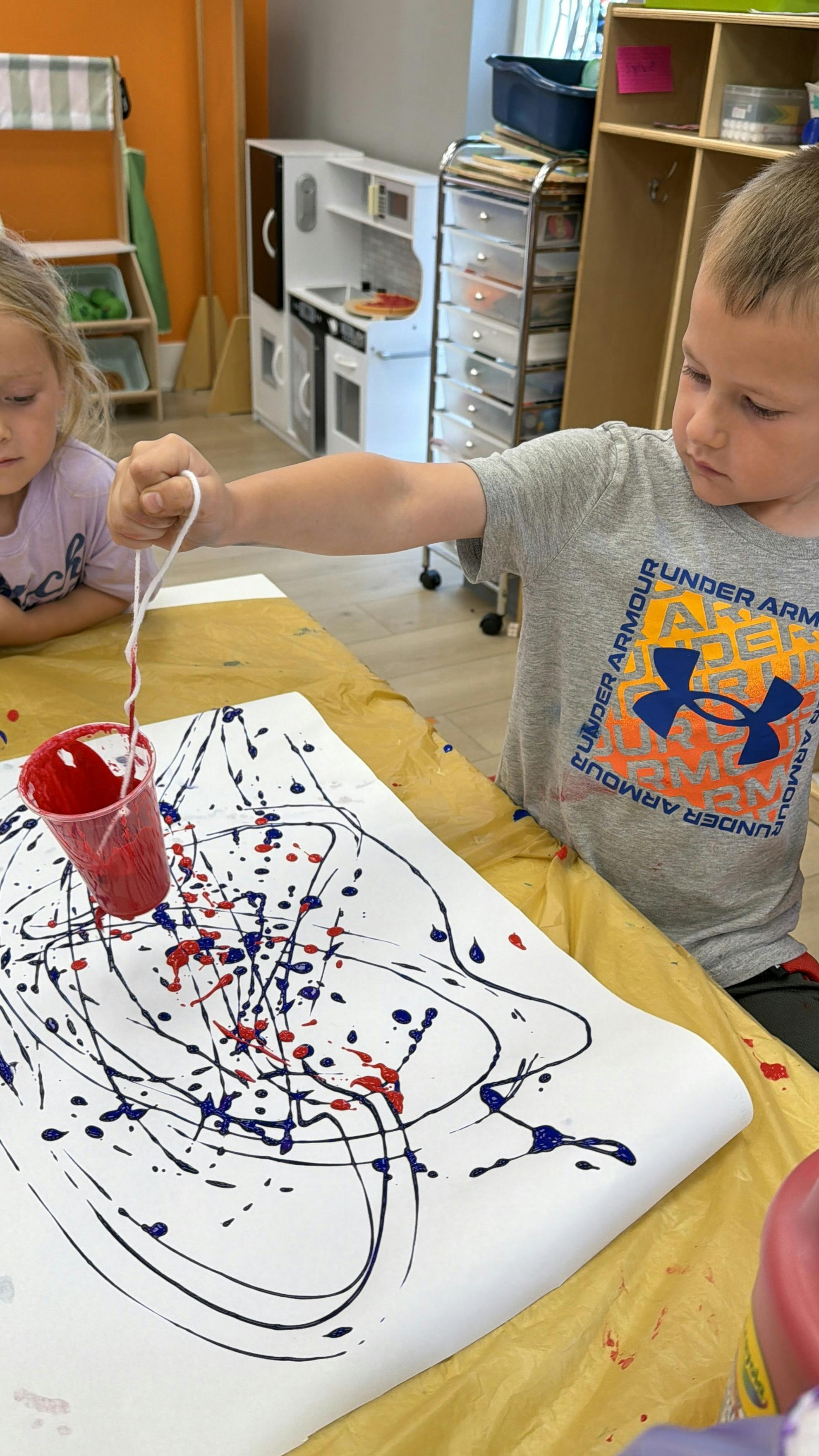 Child painting with string on paper at a table