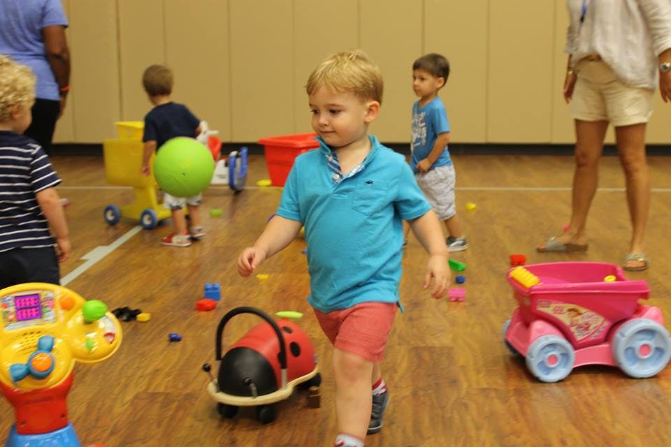 Child walking on a wooden floor with toys and other children and toys