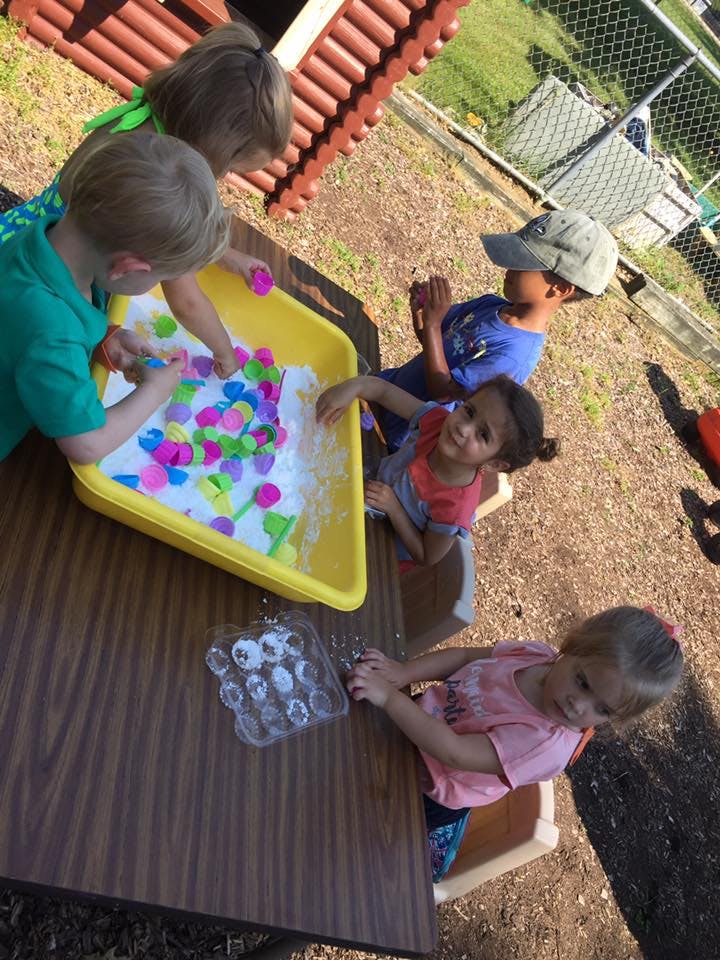 Children playing with a sensory bin filled with white material and colorful shapes