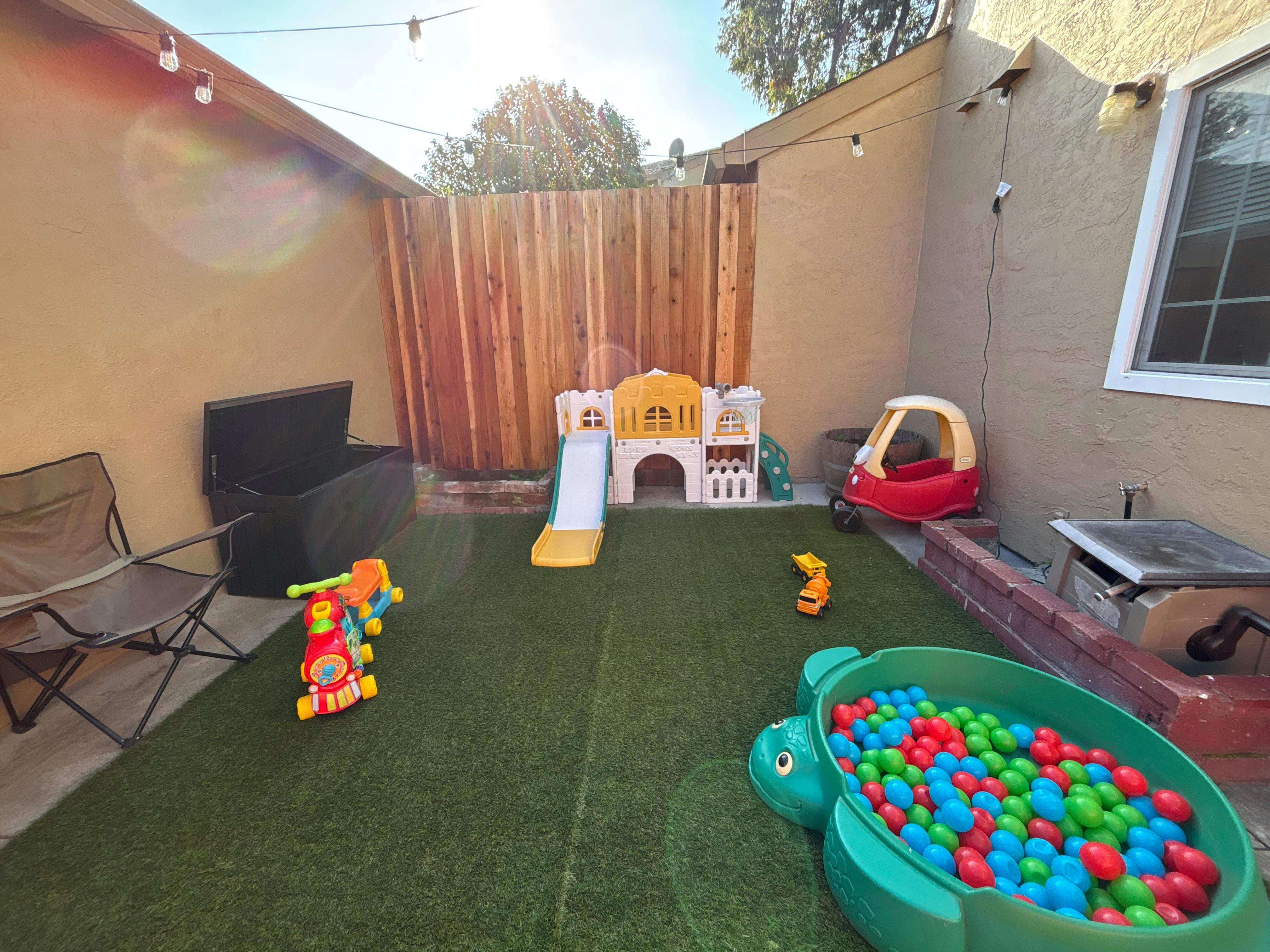 Backyard play area with a slide, ball pit, and toy car on artificial turf