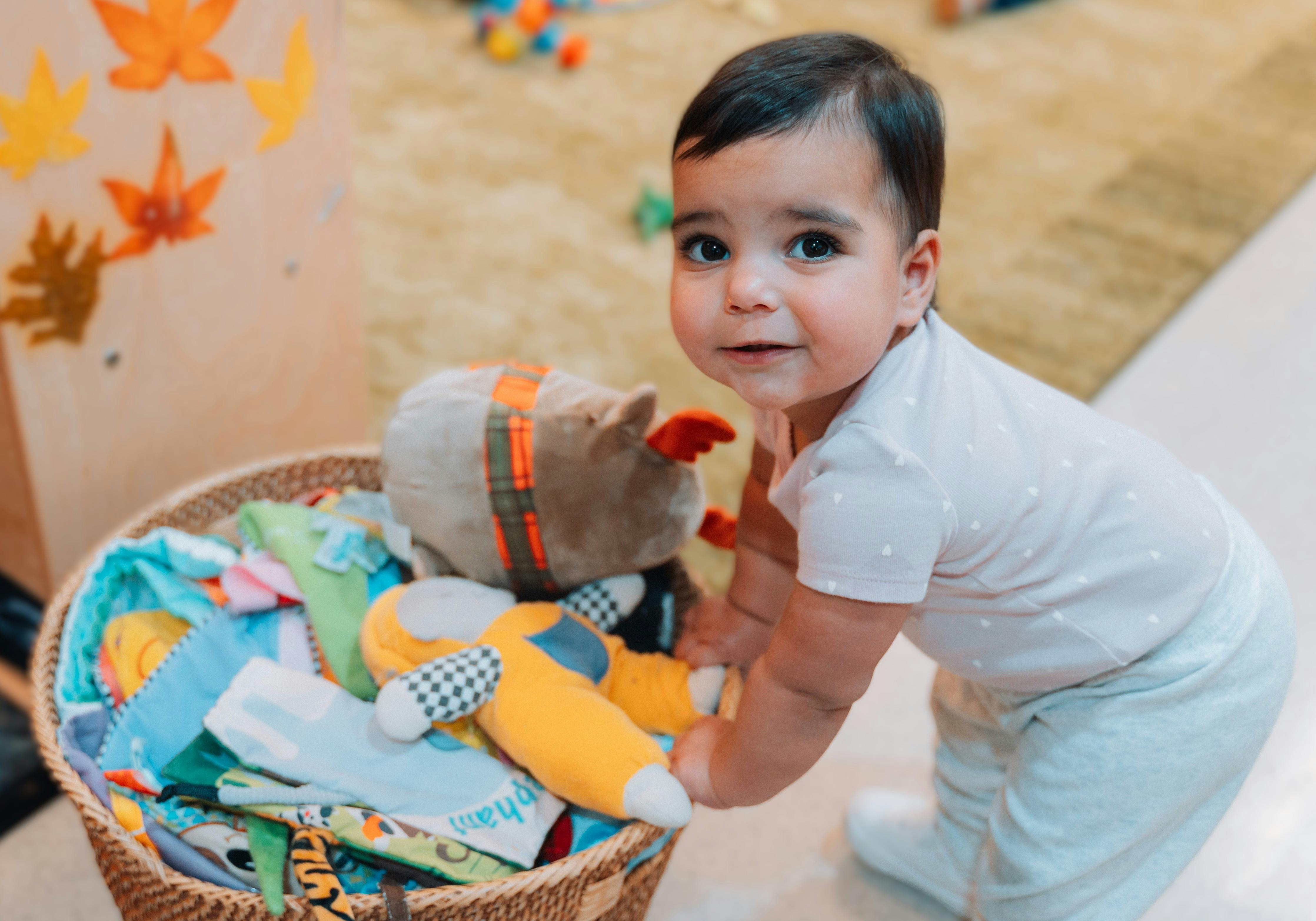 A young child standing and holding onto a basket filled with toys