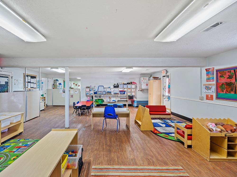 Classroom with small tables and chairs, play mats, and storage cubbies