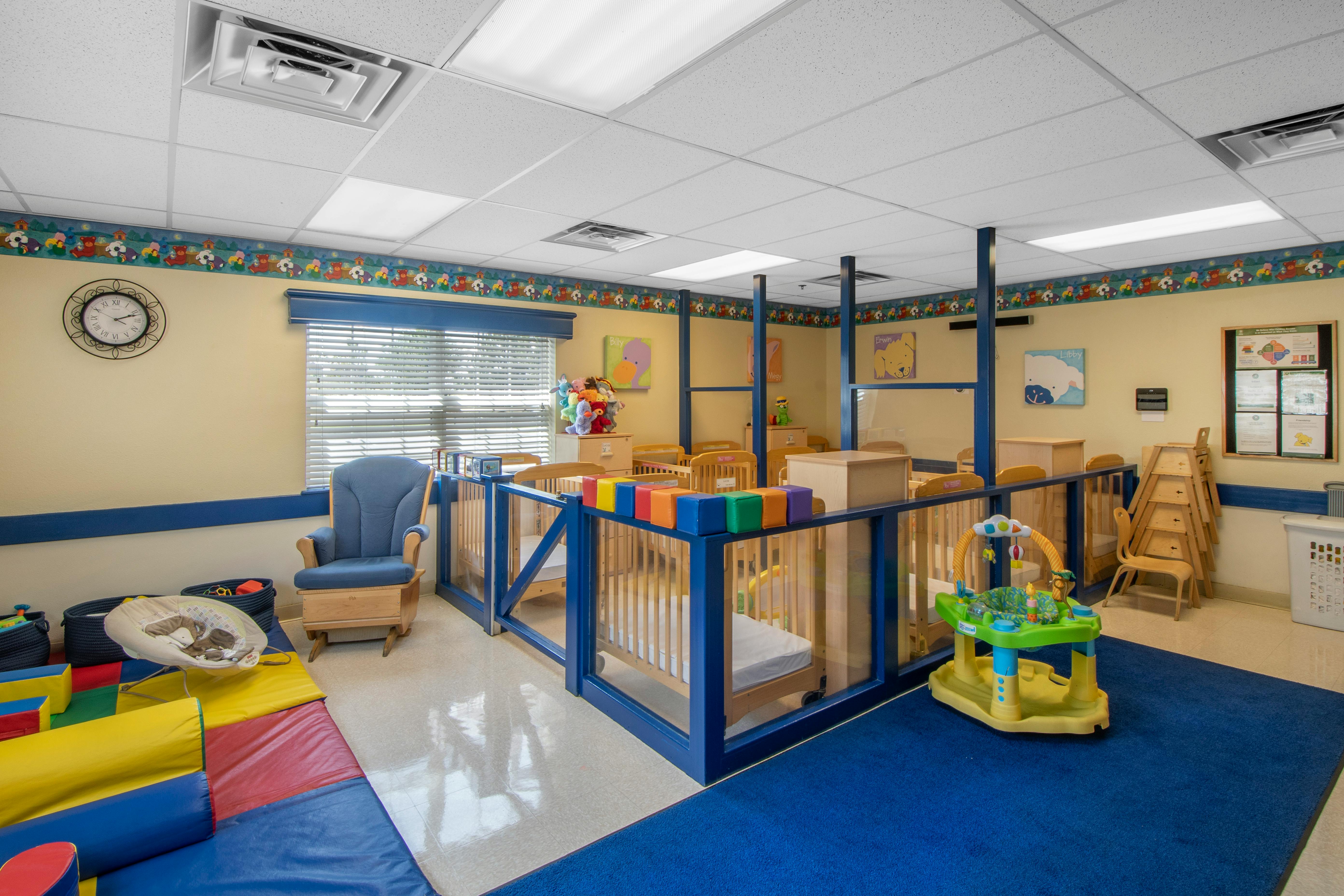 Cribs separated by blue partitions in a brightly lit daycare room