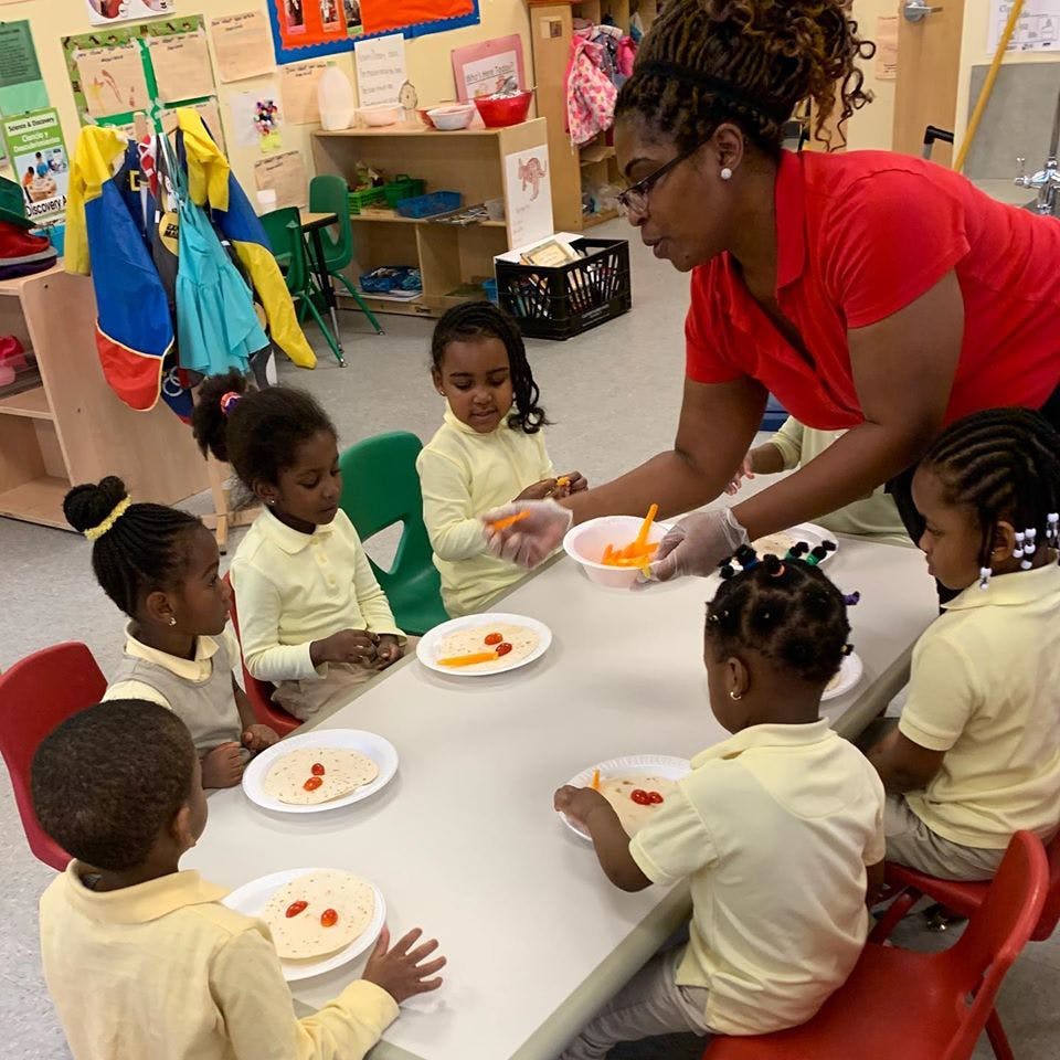 Adult serving food to children at a table in a classroom