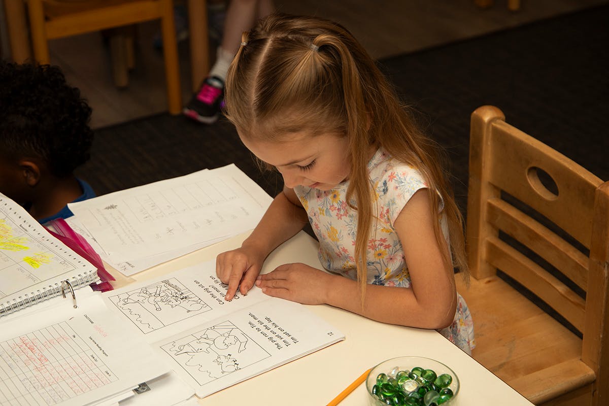 Child sitting at a desk, looking down at a book