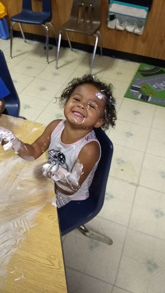 Child with white substance on face and arms at a table