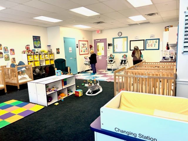 Two people in a daycare room with cribs and play mats