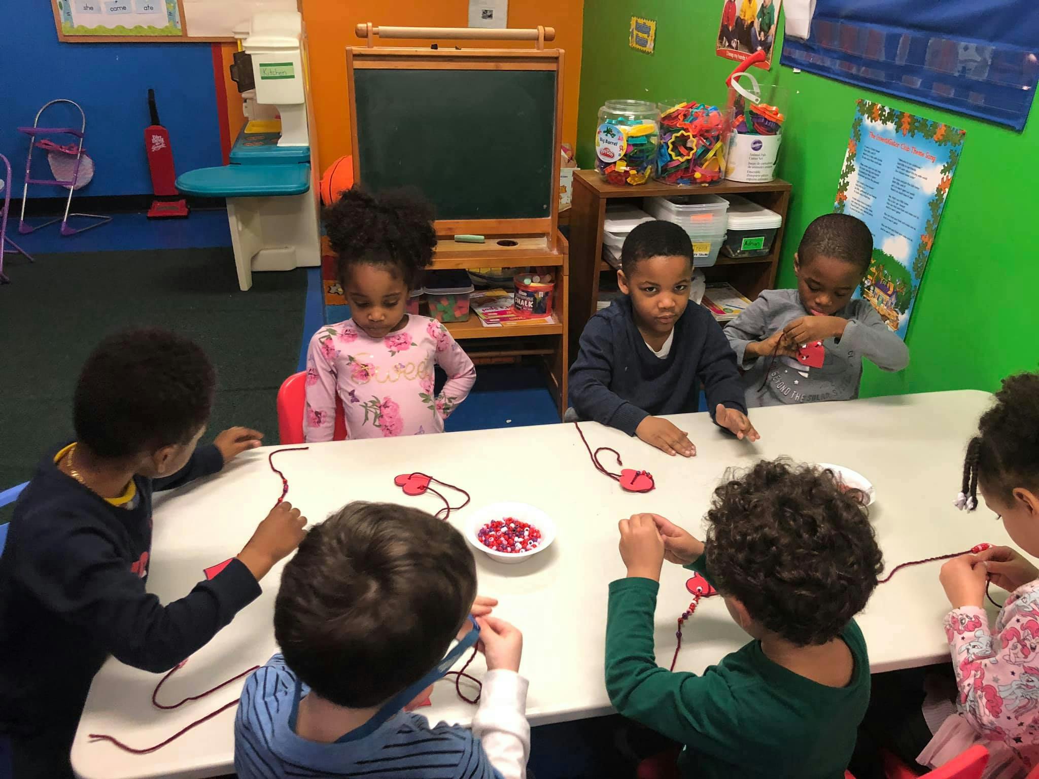Children sitting at a table doing an activity with string and red shapes