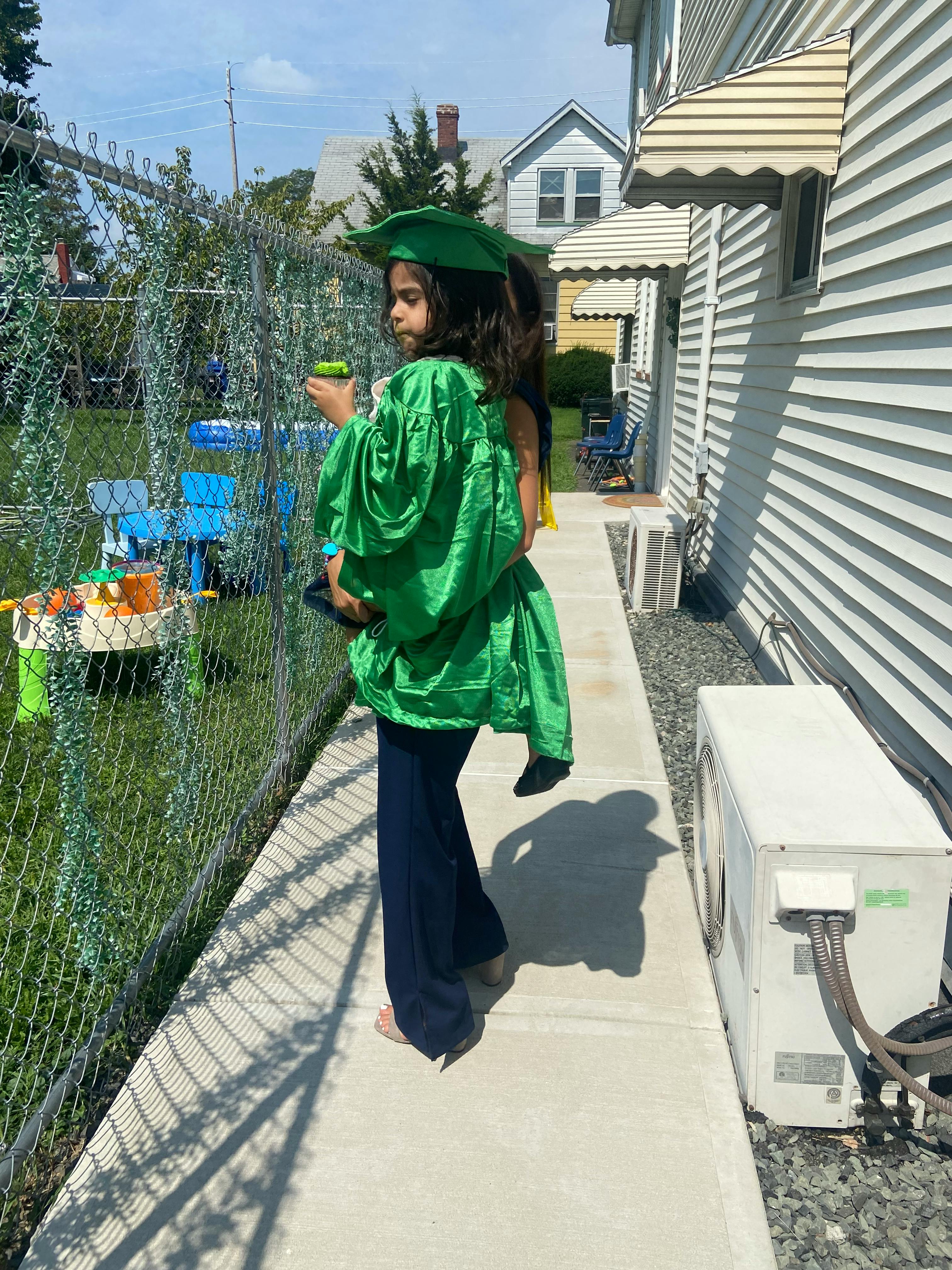 Child in a green graduation cap and gown holding a small object