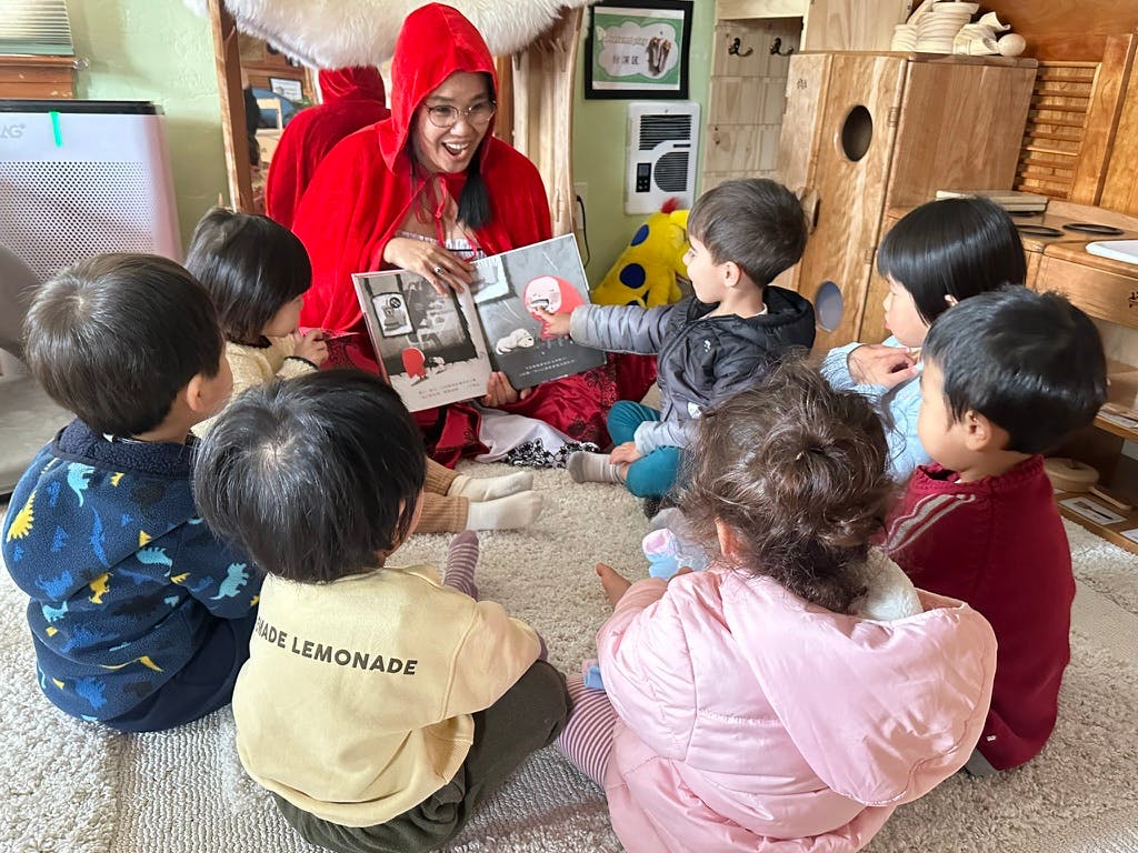 Person in red reading a book to a group of children in a classroom