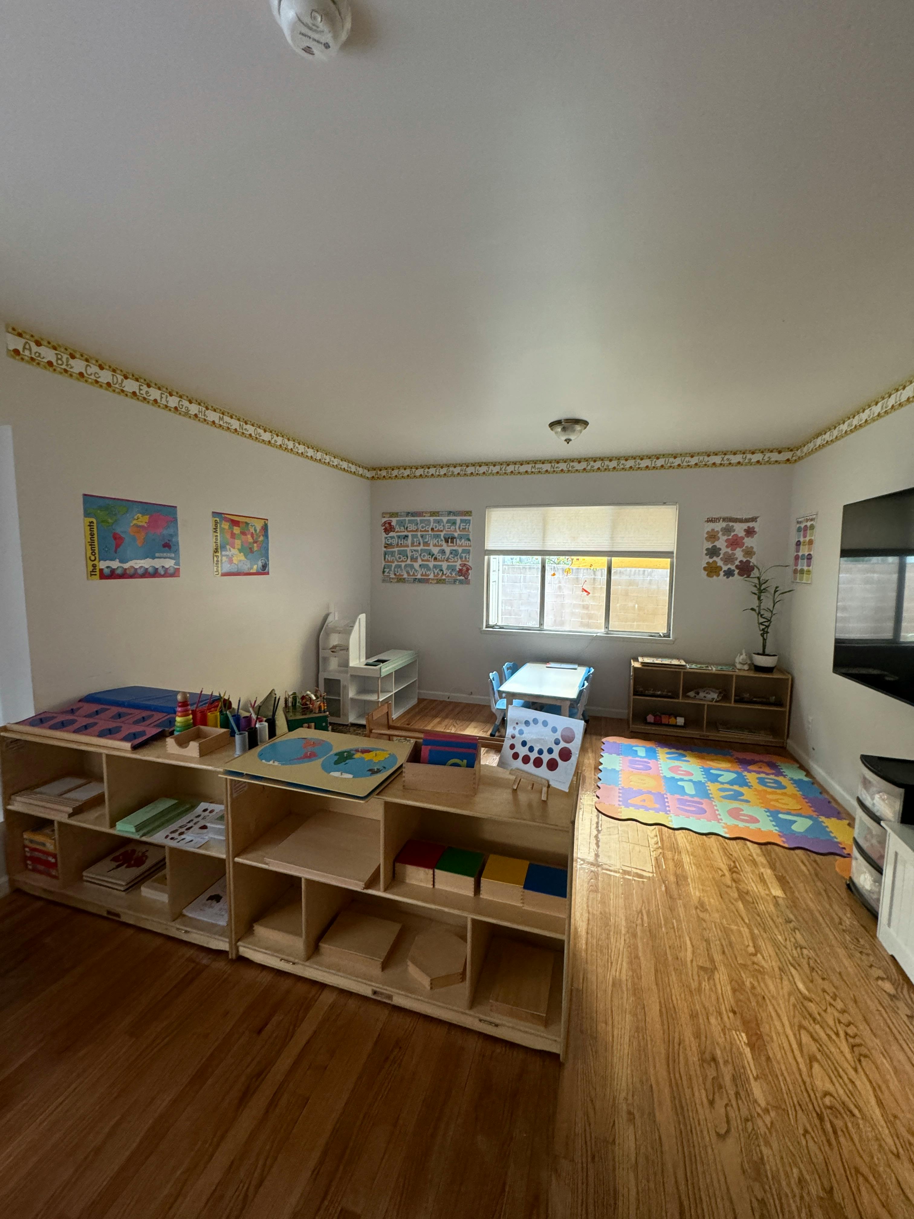 Classroom with wooden shelves, small tables, and a colorful play mat