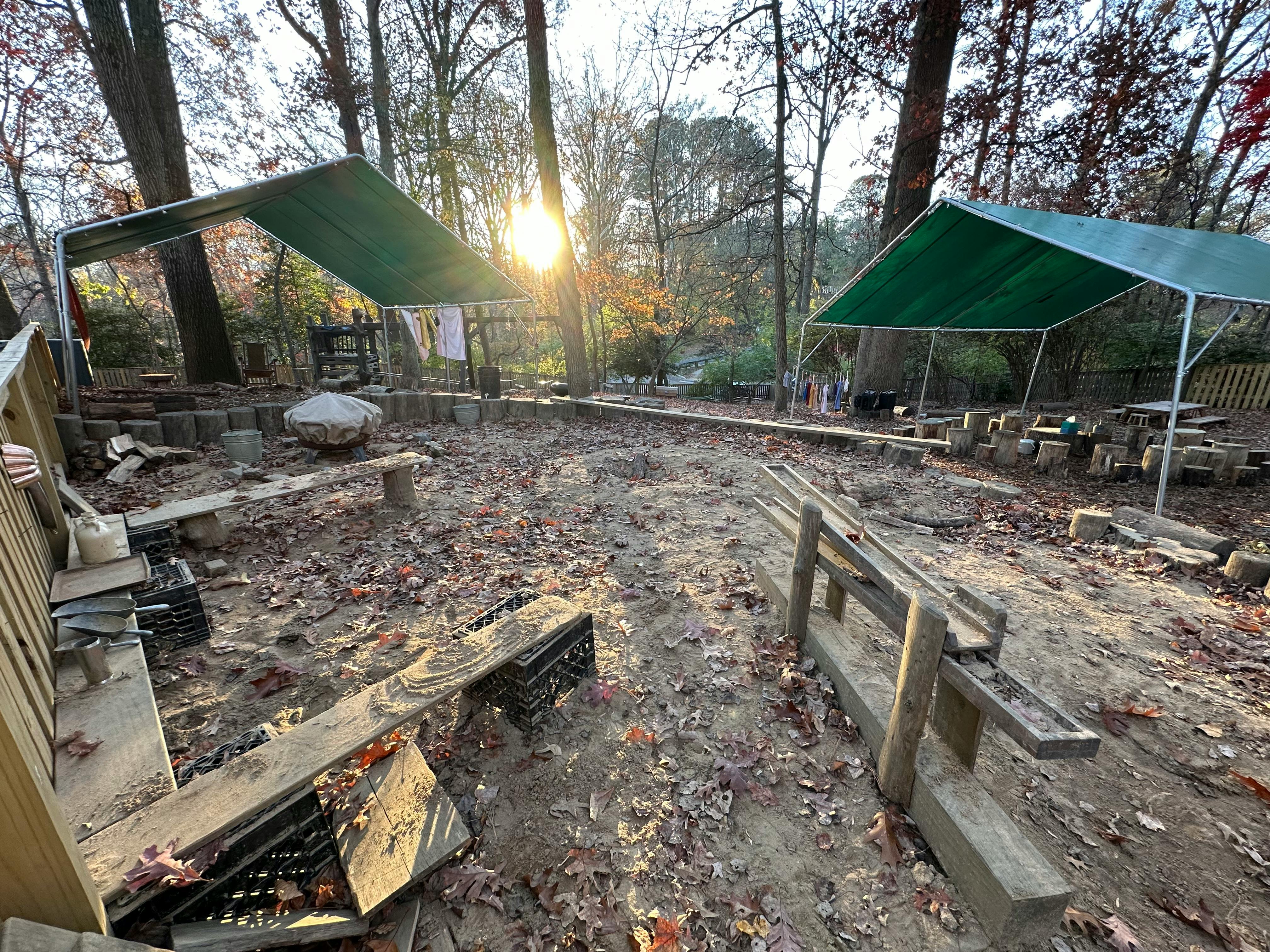 Outdoor area with two green canopies and wooden benches