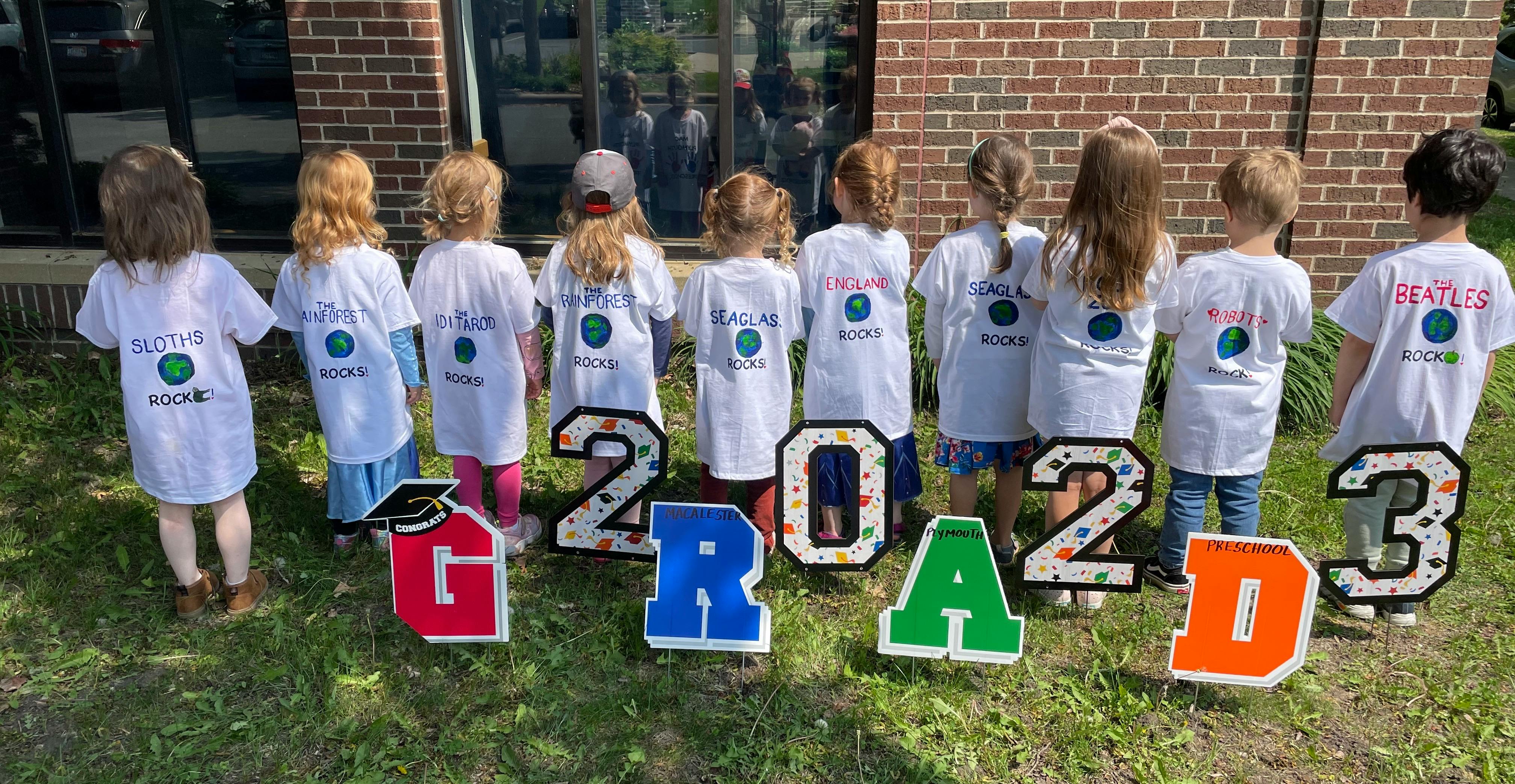 Children standing in front of large letters spelling "GRAD 2023"